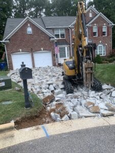 An excavator is working on a driveway in front of a house.