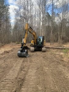 A yellow excavator on a dirt road in the woods.